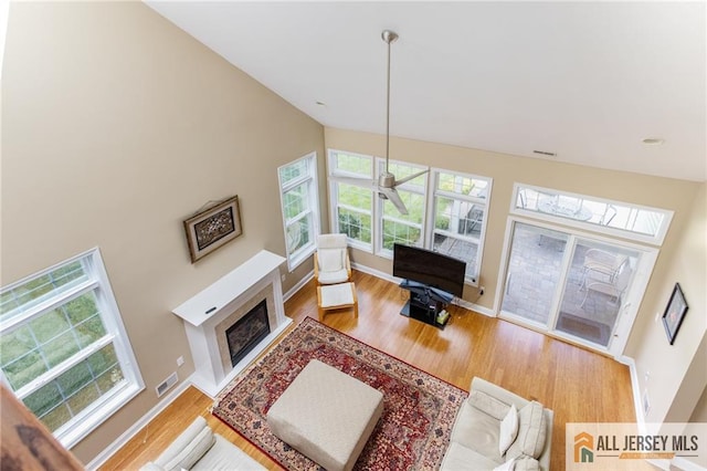 living area featuring high vaulted ceiling, a fireplace, wood finished floors, visible vents, and baseboards