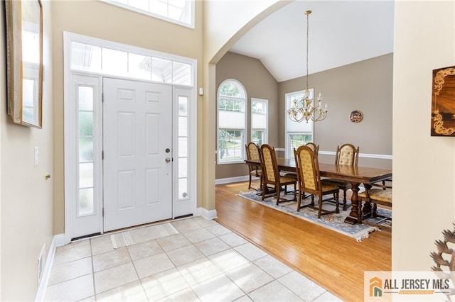 entrance foyer with arched walkways, high vaulted ceiling, light tile patterned floors, baseboards, and an inviting chandelier