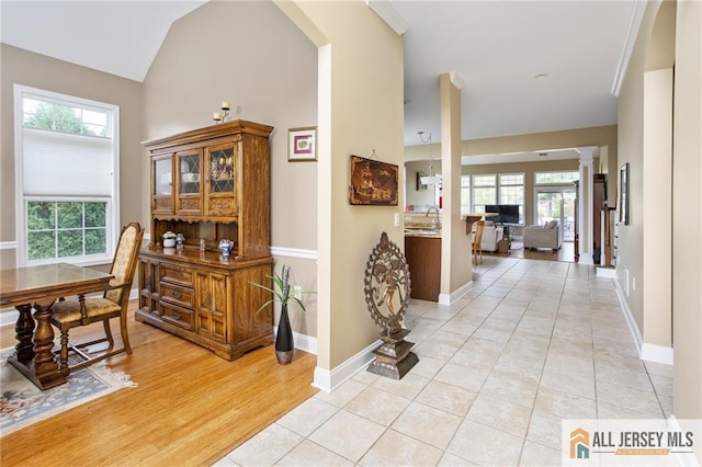 hallway featuring ornate columns, plenty of natural light, light tile patterned floors, and vaulted ceiling