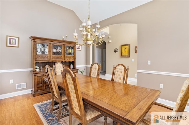 dining space with lofted ceiling, arched walkways, visible vents, light wood-style floors, and an inviting chandelier