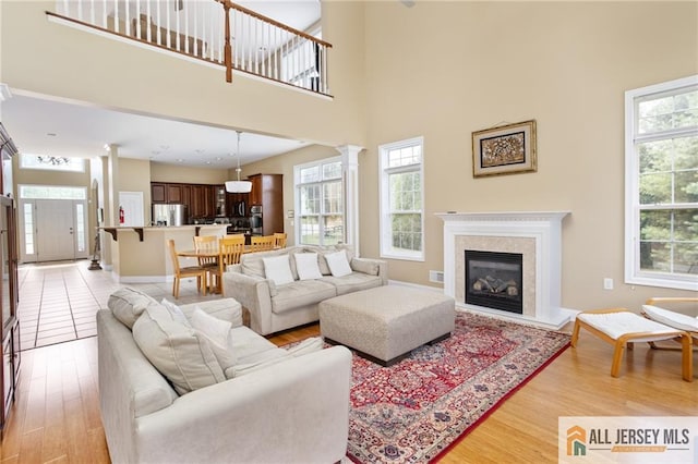 living room with a premium fireplace, a towering ceiling, light wood-style flooring, and ornate columns