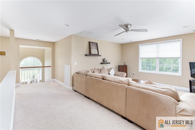 living area featuring a healthy amount of sunlight, light colored carpet, ceiling fan, and baseboards