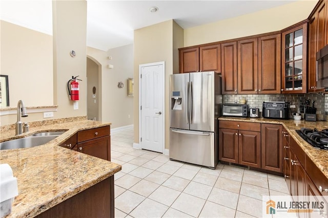 kitchen featuring light tile patterned floors, light stone counters, a sink, stainless steel refrigerator with ice dispenser, and backsplash