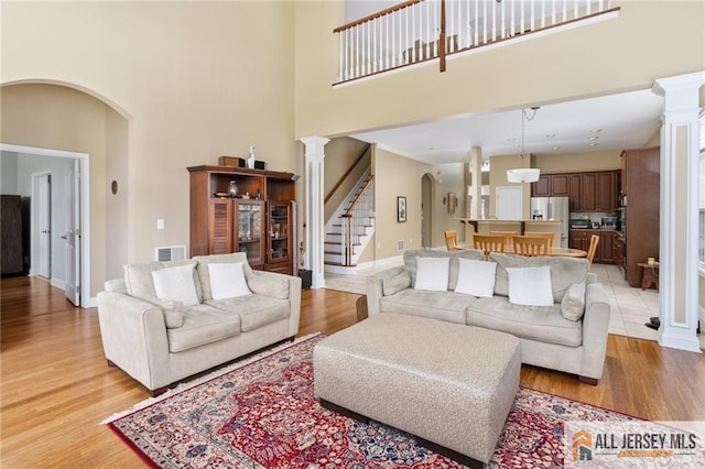 living area with arched walkways, light wood finished floors, stairway, and visible vents