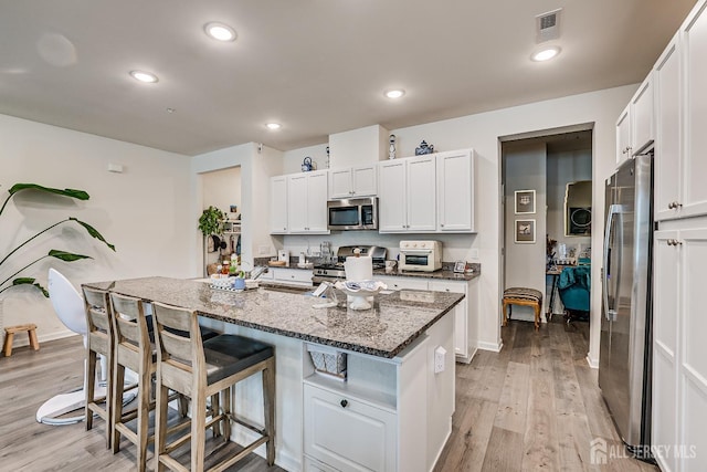 224 Park Ln, Dunellen, NJ 08812 - kitchen featuring appliances with stainless steel finishes, a kitchen breakfast bar, light wood-style flooring, dark stone counters, and white cabinetry