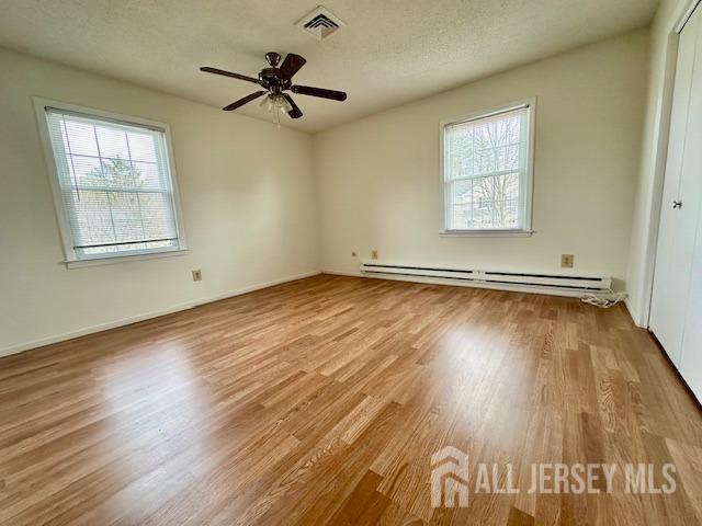 unfurnished room featuring a baseboard heating unit, plenty of natural light, wood finished floors, and visible vents