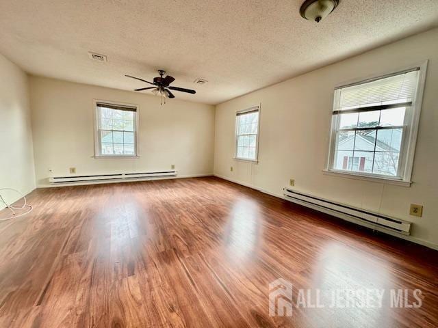 spare room featuring a textured ceiling, baseboard heating, wood finished floors, and visible vents