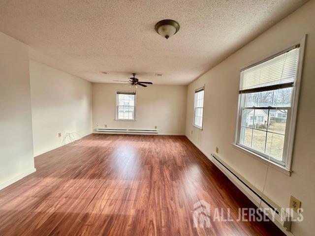 empty room featuring ceiling fan, a textured ceiling, a baseboard heating unit, and wood finished floors