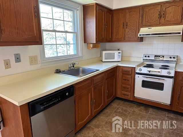 kitchen with white appliances, a sink, light countertops, range hood, and brown cabinets