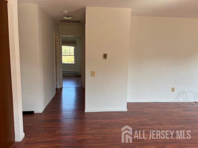 hall with a baseboard radiator, visible vents, baseboards, and wood finished floors