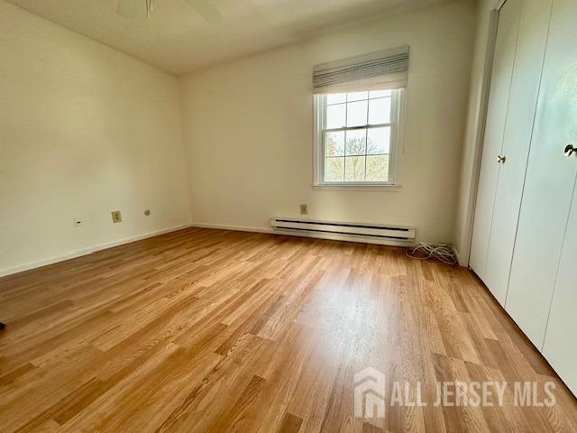 unfurnished bedroom featuring light wood-style floors, a baseboard heating unit, and a ceiling fan