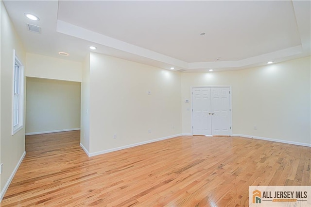 unfurnished room featuring a tray ceiling, light wood-style flooring, recessed lighting, and baseboards