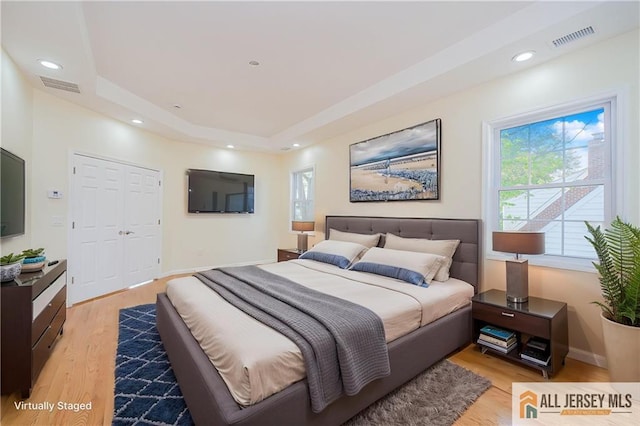 bedroom with light wood-type flooring, a raised ceiling, baseboards, and recessed lighting