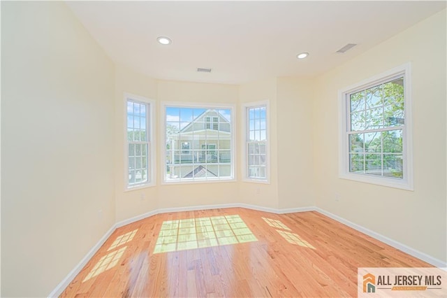 empty room with healthy amount of natural light, baseboards, light wood-type flooring, and recessed lighting