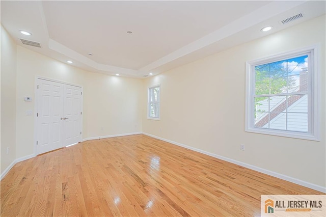 unfurnished room featuring light wood finished floors, a raised ceiling, baseboards, and recessed lighting