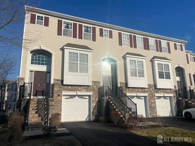 multi unit property featuring stone siding, an attached garage, and driveway