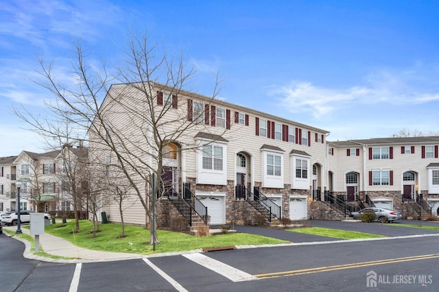 townhome / multi-family property with stone siding, an attached garage, and stairs