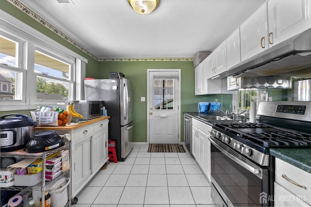 kitchen featuring stainless steel appliances, a sink, white cabinetry, light tile patterned floors, and under cabinet range hood