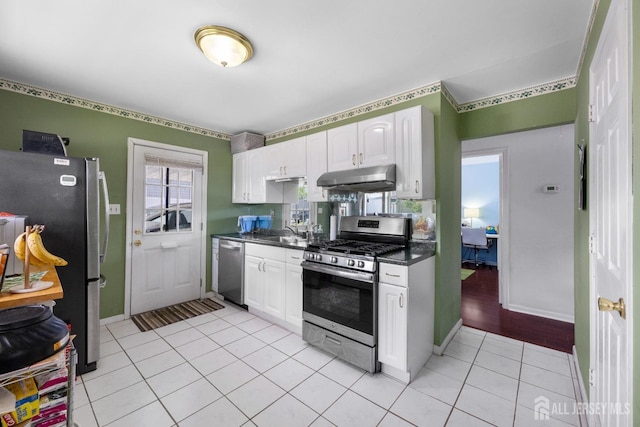 kitchen with stainless steel appliances, under cabinet range hood, dark countertops, white cabinets, and a sink