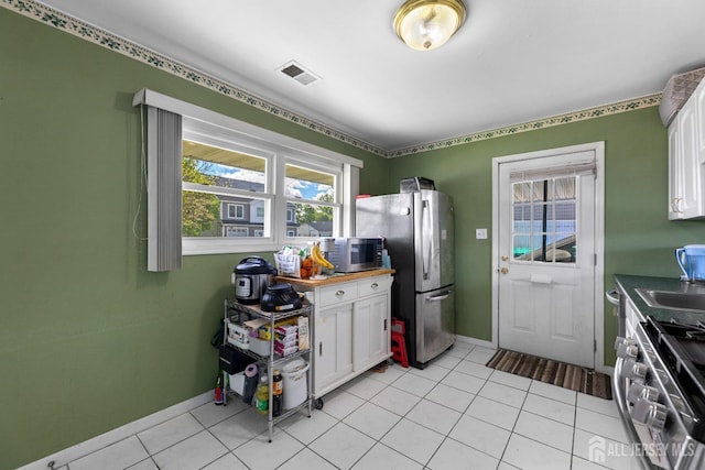 kitchen with appliances with stainless steel finishes, white cabinets, baseboards, and light tile patterned flooring