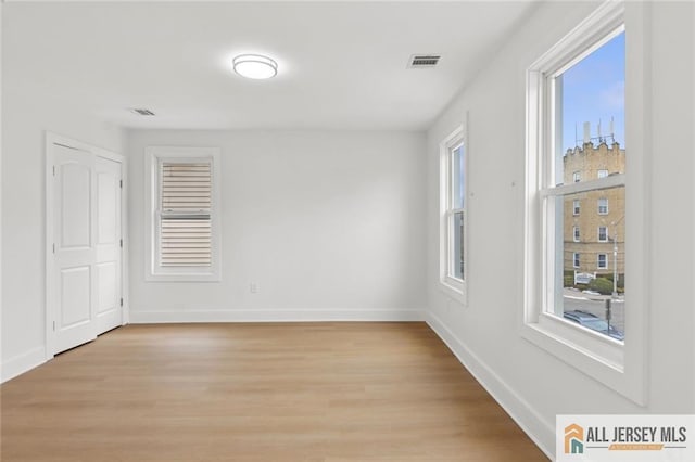 spare room featuring light wood-style flooring, visible vents, and baseboards