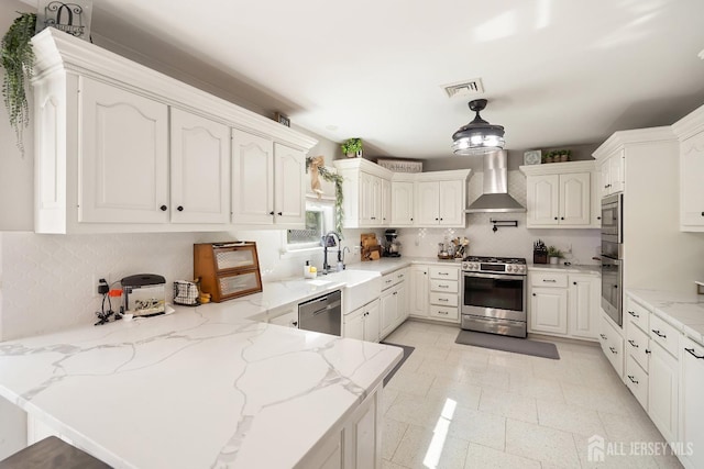 242 Green St, Old Bridge, NJ 08857 - kitchen featuring wall chimney exhaust hood, stainless steel appliances, a peninsula, decorative backsplash, and light stone counters
