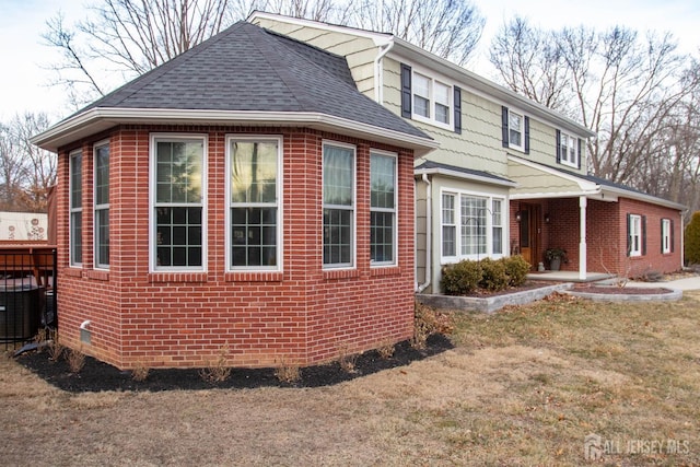 view of property exterior with central AC unit, brick siding, and a shingled roof