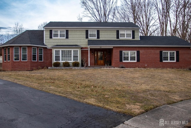 traditional-style house with brick siding, a shingled roof, and a front yard