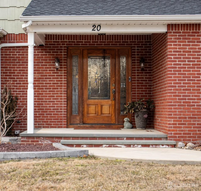 doorway to property with brick siding and a shingled roof