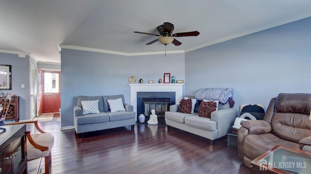 living room with dark wood-style flooring, a glass covered fireplace, a ceiling fan, and crown molding