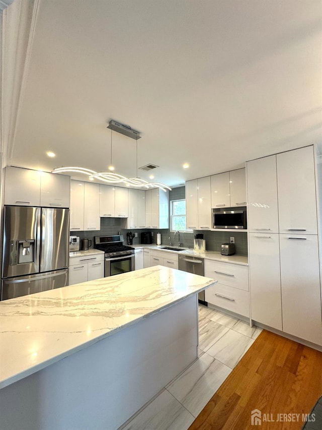 12 Yates Ave, South River, NJ 08882 - kitchen with stainless steel appliances, modern cabinets, white cabinetry, light stone countertops, and decorative light fixtures
