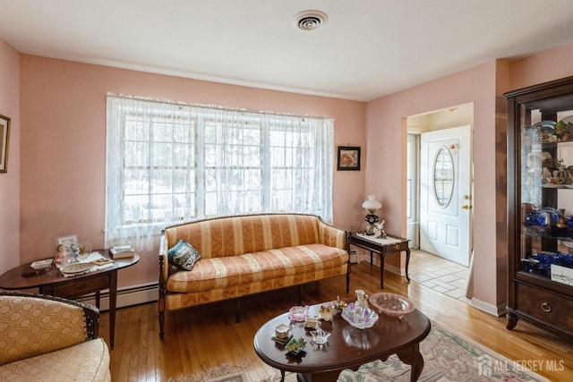 living room with light wood-type flooring, visible vents, baseboard heating, and baseboards