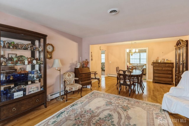 dining room with a baseboard heating unit, visible vents, a chandelier, and wood finished floors