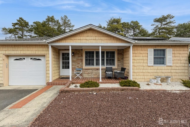 ranch-style home featuring driveway, solar panels, stone siding, an attached garage, and a porch