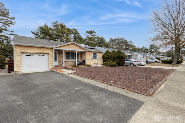 ranch-style home with a garage, solar panels, driveway, stone siding, and roof with shingles