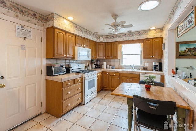 kitchen featuring tile countertops, light tile patterned floors, white appliances, a sink, and decorative backsplash