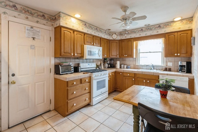 kitchen with light tile patterned flooring, white appliances, a sink, tile counters, and tasteful backsplash