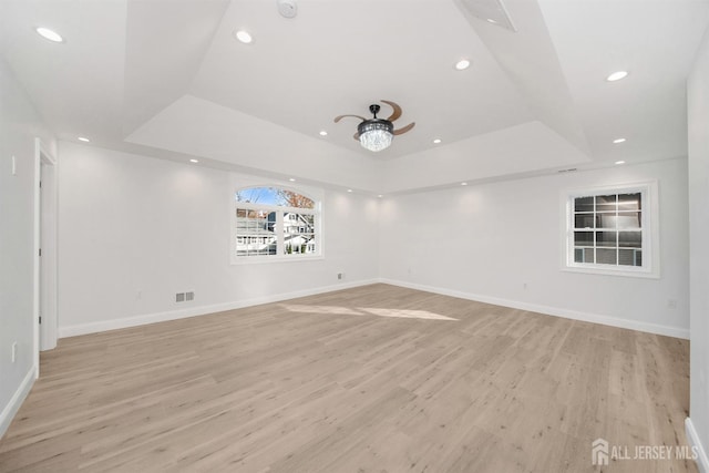 empty room featuring a tray ceiling, visible vents, light wood finished floors, and recessed lighting