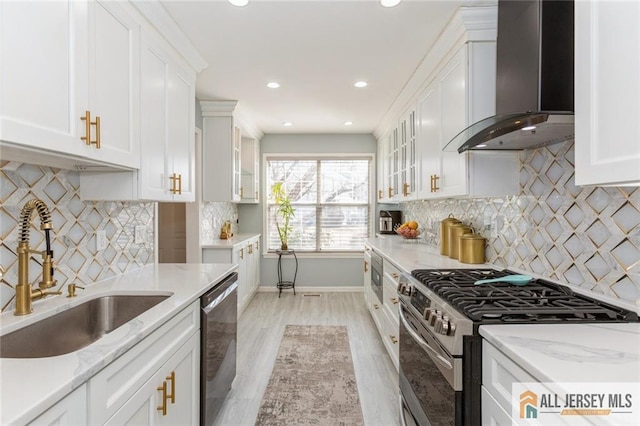 kitchen with a sink, stainless steel appliances, wall chimney exhaust hood, white cabinets, and glass insert cabinets