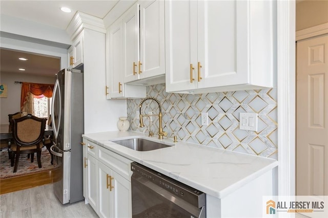 kitchen featuring light stone countertops, freestanding refrigerator, a sink, white cabinets, and dishwasher