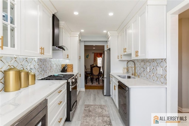 kitchen featuring a sink, stainless steel appliances, light wood-style floors, wall chimney exhaust hood, and white cabinets