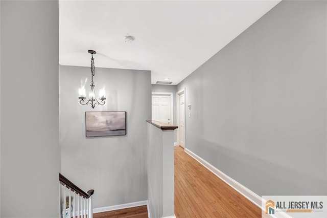 hall featuring an inviting chandelier, baseboards, wood finished floors, and an upstairs landing