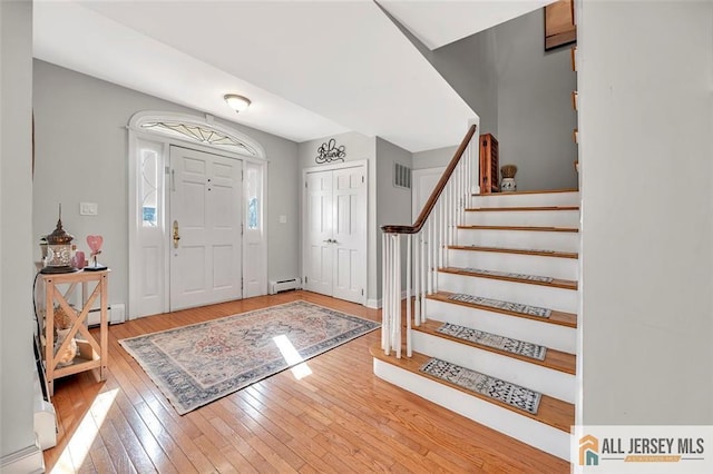 foyer with a baseboard heating unit, wood finished floors, visible vents, stairs, and baseboard heating