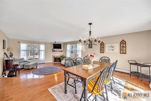 dining area featuring a notable chandelier, a fireplace, baseboards, and light wood-style floors