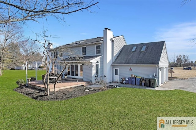 rear view of house featuring driveway, a garage, a shingled roof, a chimney, and a yard