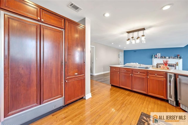 kitchen with wine cooler, decorative light fixtures, light countertops, visible vents, and light wood-style flooring