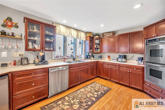 kitchen with appliances with stainless steel finishes, light wood-style floors, light countertops, and a sink