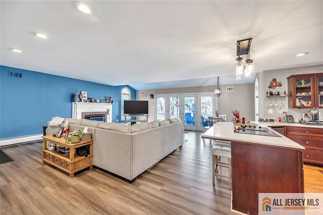 living room featuring light wood finished floors, a baseboard radiator, visible vents, and a brick fireplace