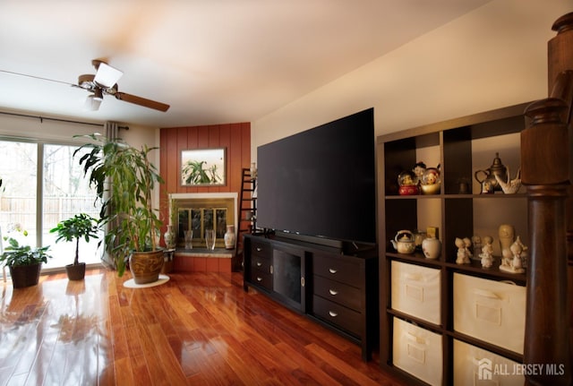 living room with a glass covered fireplace, ceiling fan, and wood finished floors