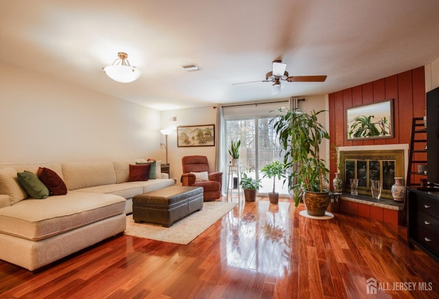 living area with a ceiling fan, visible vents, a fireplace, and wood finished floors